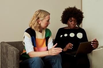 Two women sitting on a sofa looking at a laptop