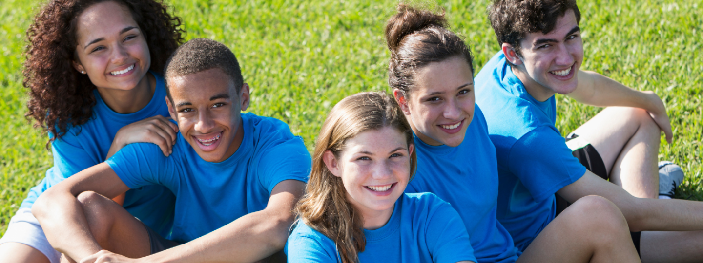 Groups of five teenagers wearing blue tee-shirts sitting on the grass