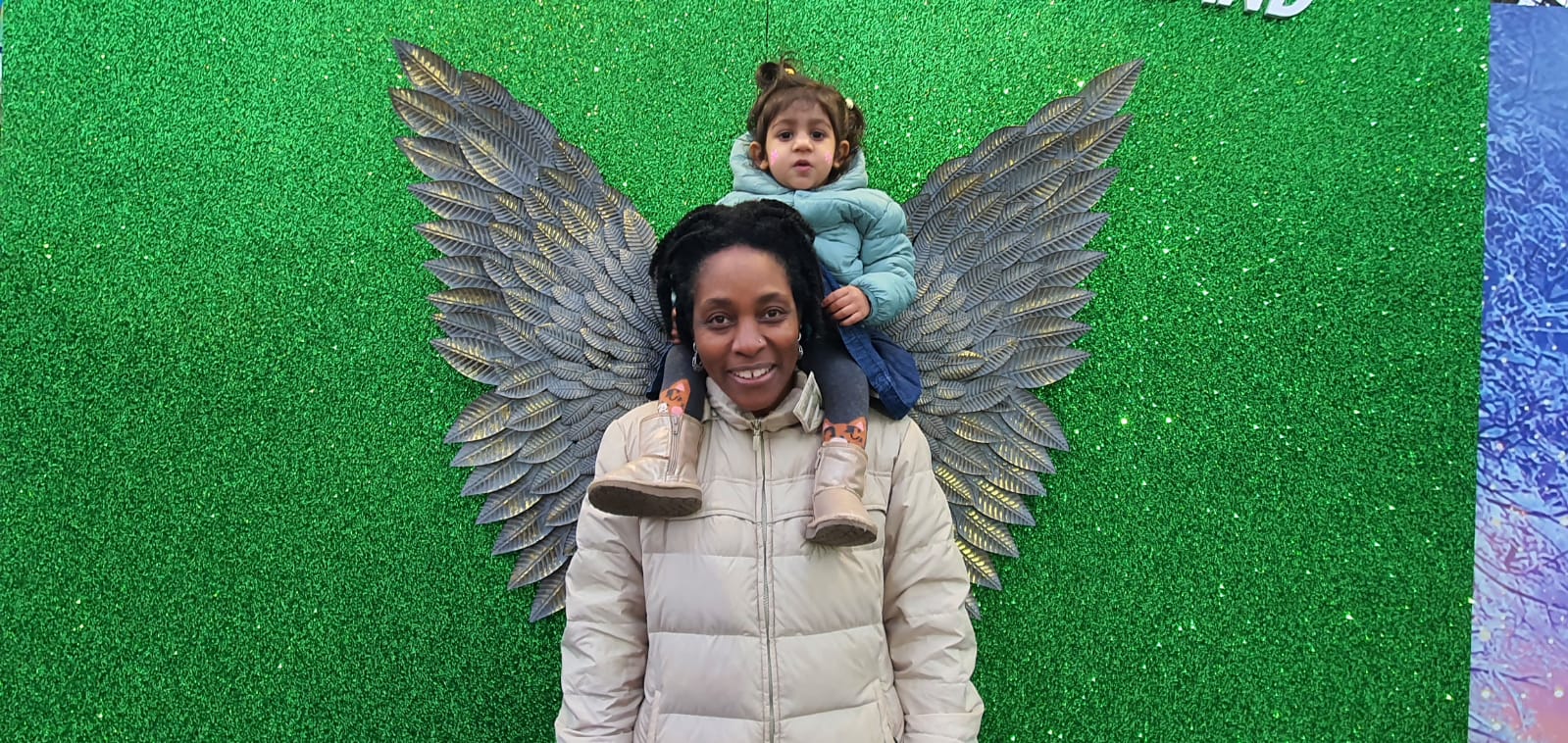 smiling woman with child sitting on her shoulders in front of an image of angel wings