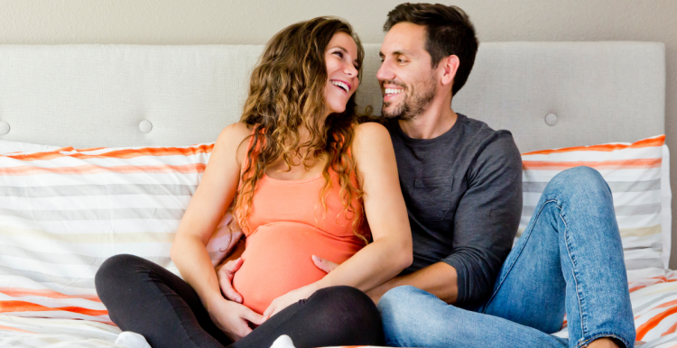 photo of man and pregnant woman sitting on a bed smiling