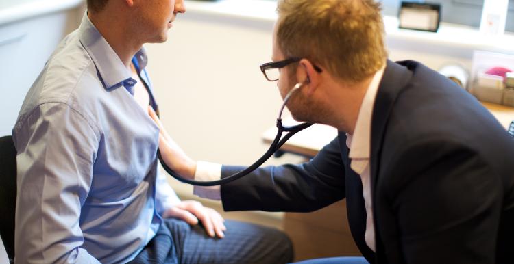 male GP checking the chest if a male patient with a stethoscope