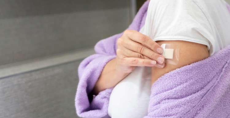 A woman in a purple bath robe places a HRT patch on her arm.