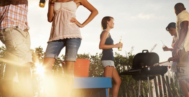 group of young people holding drinks and having a barbecue in a garden