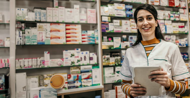 female pharmacist holding an iPad standing in front of shelves of medication