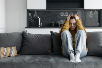 Young woman sitting on sofa with her head in her hands