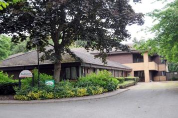 Croftwood Care Home main building, with large tree and bushes in front of single storey building