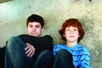 Two boys, sitting on the floor against a wall, looking into the camera