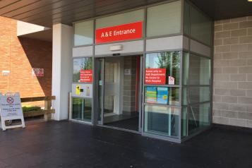 The entrance to A&E at Whiston Hospital.  Red A&E entrance sign above glass sliding doors 