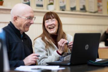 two people smiling using a laptop. Ageing Better partnered with Independent Age to release new age-positive image library photos that better represent the diversity of people aged 50+ in England.