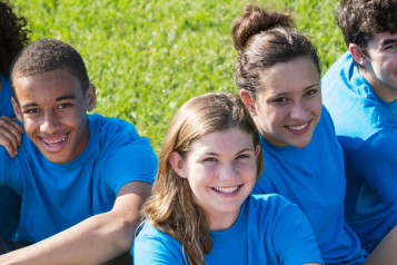 Groups of five teenagers wearing blue tee-shirts sitting on the grass