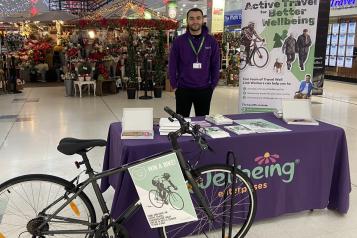 Photograph of Active travel stall at Runcorn Shopping City, with Wellbeing staff member and bike. 