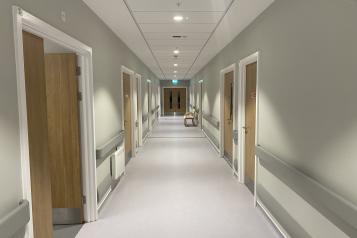 image of a hospital corridor. Doors on left and right side with double swing doors in the distance.