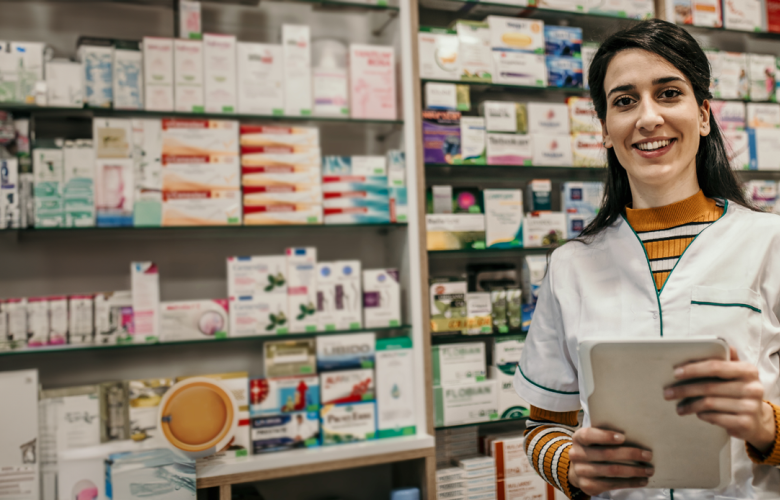 female pharmacist holding an iPad standing in front of shelves of medication