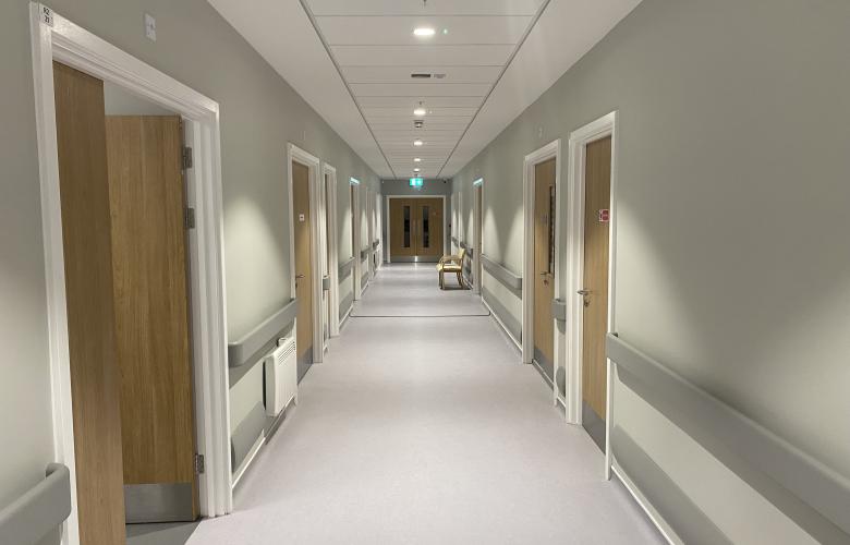 image of a hospital corridor. Doors on left and right side with double swing doors in the distance.