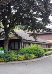 Croftwood Care Home main building, with large tree and bushes in front of single storey building